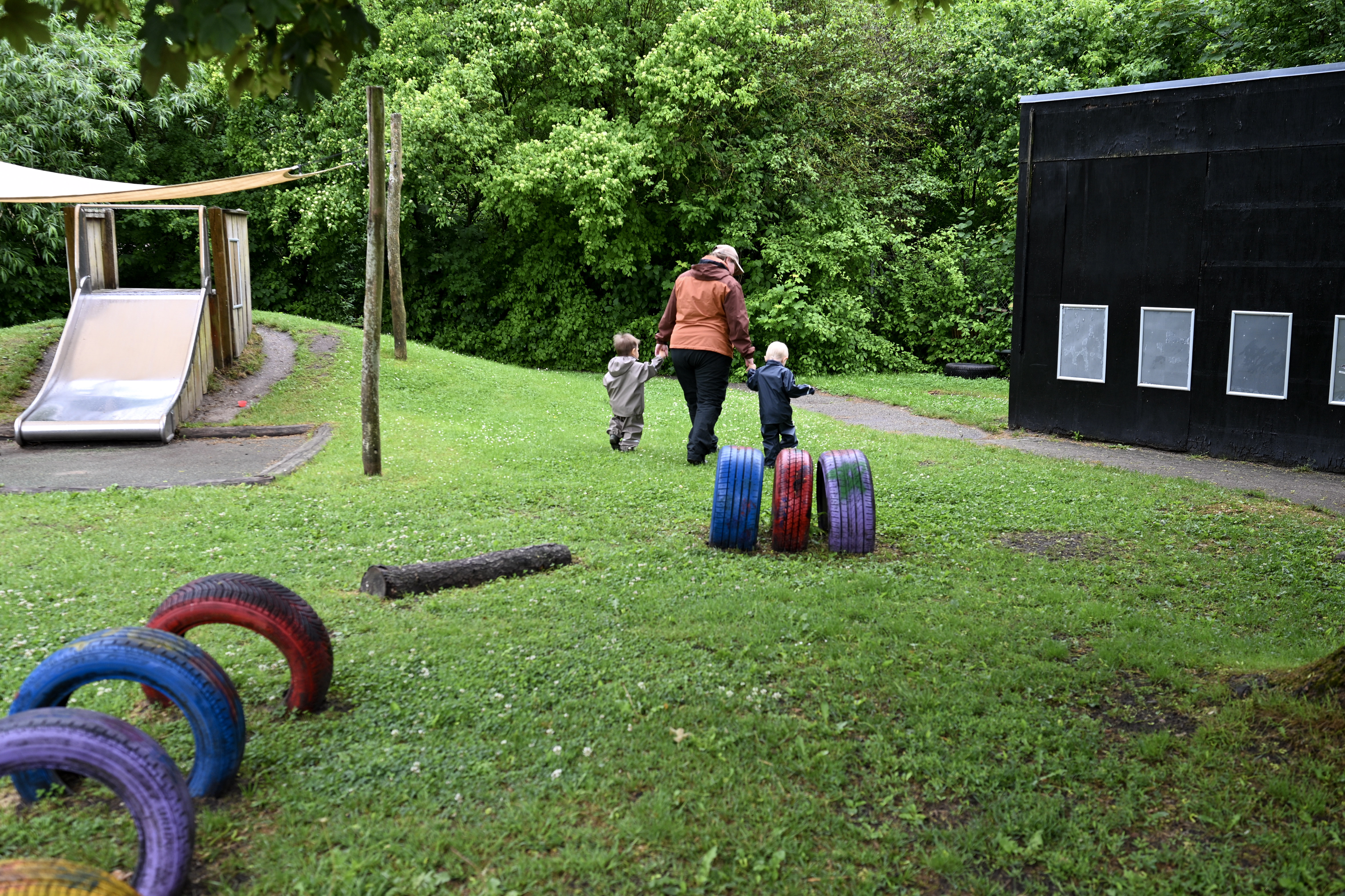 Voksen med et barn i hver hånd på legeplads